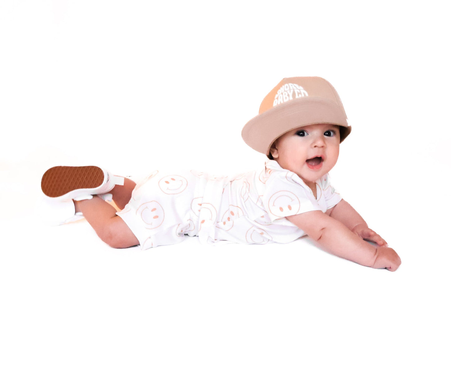 Photo of a baby boy wearing a white shirt and shorties set adorned with camel-colored smiley faces, ideal for toddlers. The design features ribbed bamboo fabric, ensuring comfort and breathability. Available sizes include 3-6 months, 6-12 months, 12-18 months, and 18-24 months, making it a versatile and stylish choice for both boys and girls.