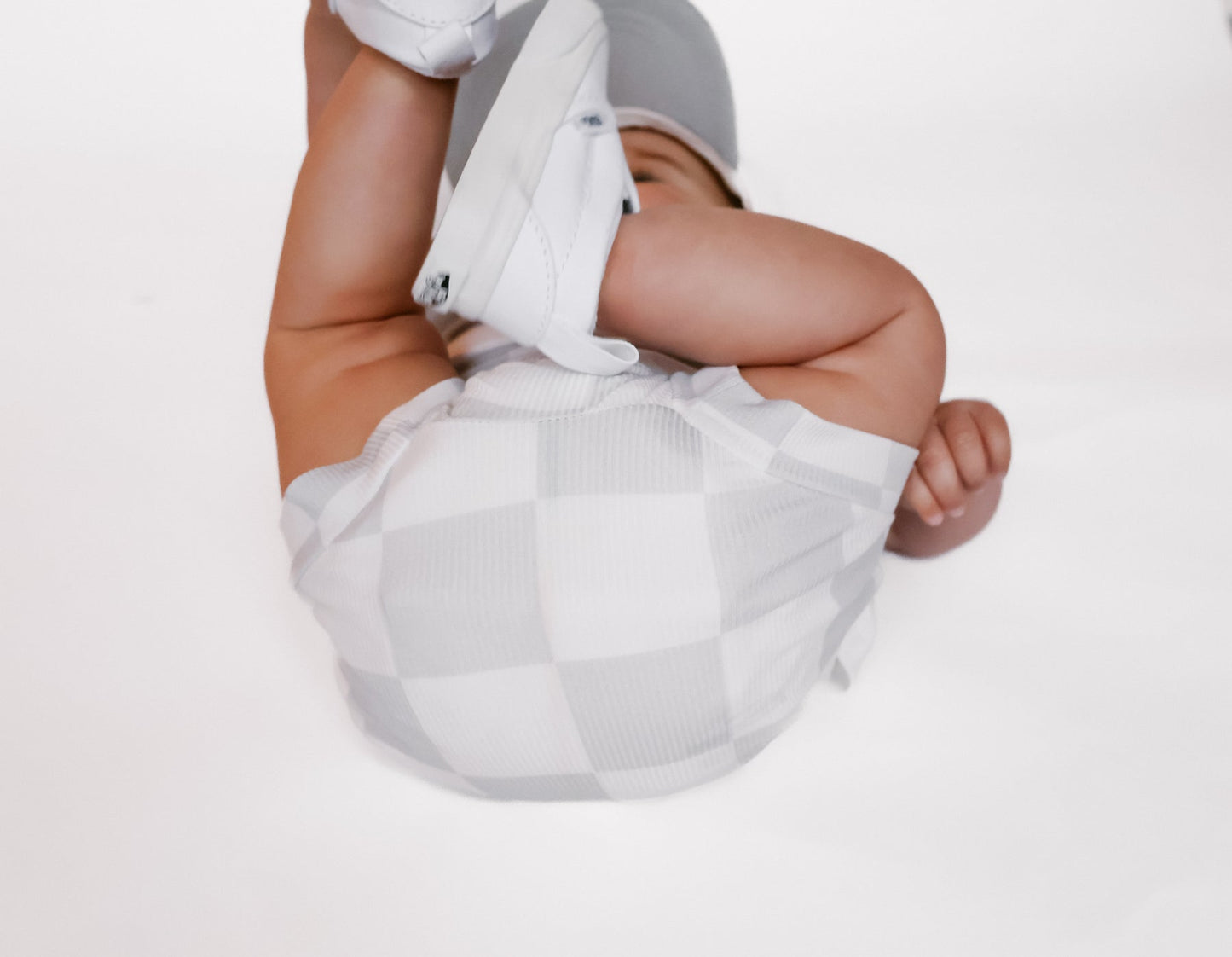 Photo of a baby boy wearing a stylish grey and white checkered shirt and shorties set for toddlers. The design features a ribbed bamboo fabric, offering comfort and breathability. Available in sizes 3-6 months, 6-12 months, 12-18 months, and 18-24 months, this outfit is perfect for both boys and girls, combining trendy patterns with eco-friendly materials.