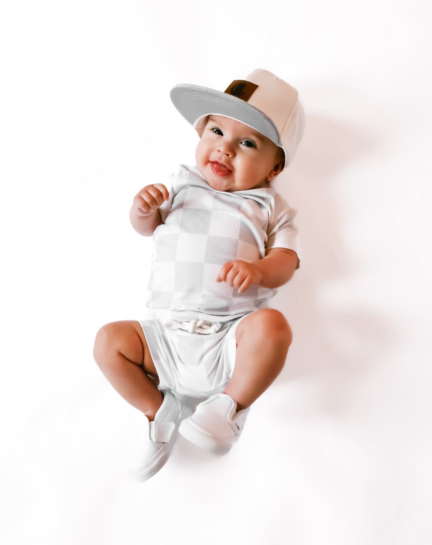 Photo of a baby boy wearing a stylish grey and white checkered shirt and shorties set for toddlers. The design features a ribbed bamboo fabric, offering comfort and breathability. Available in sizes 3-6 months, 6-12 months, 12-18 months, and 18-24 months, this outfit is perfect for both boys and girls, combining trendy patterns with eco-friendly materials.