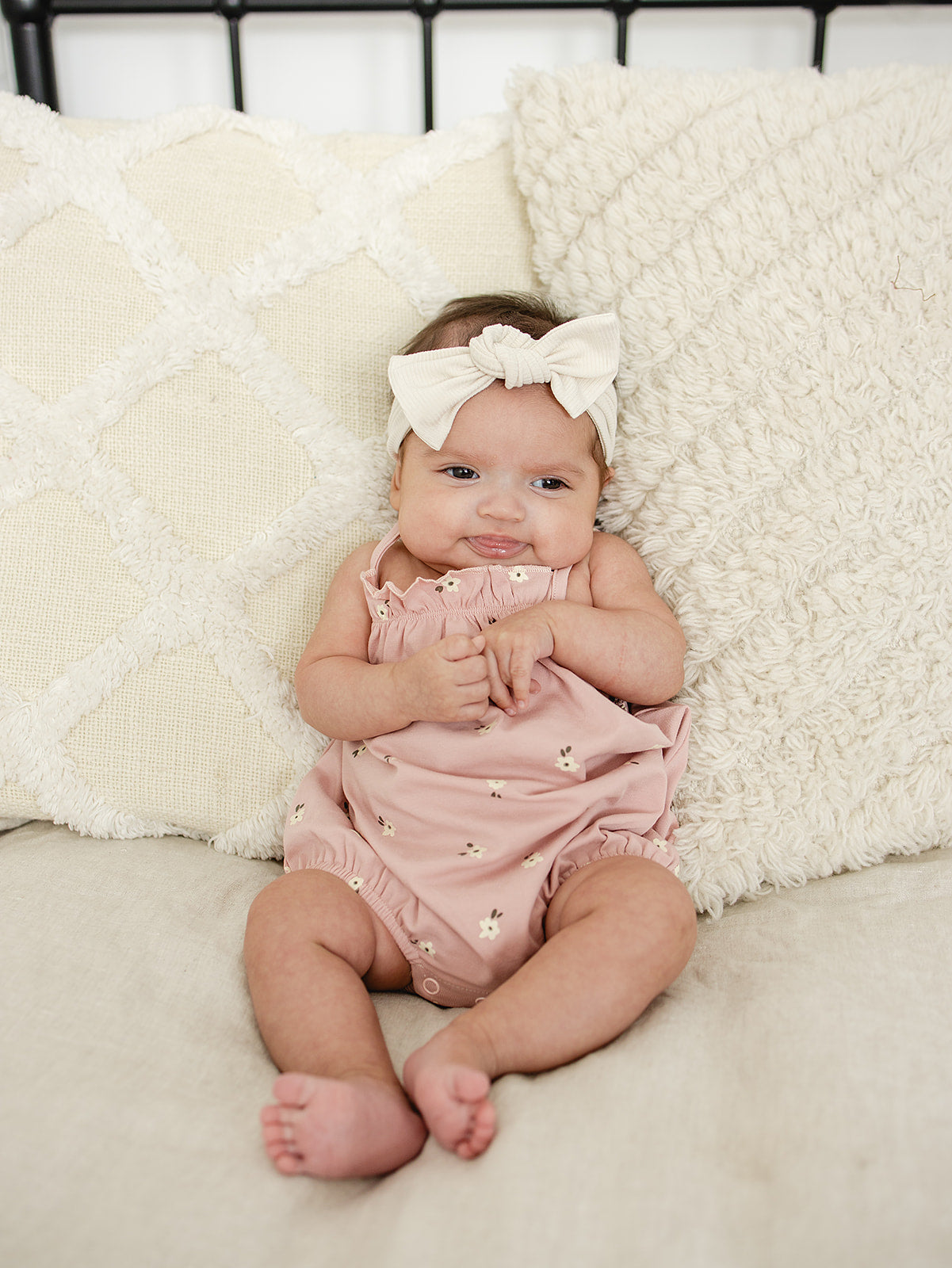 Baby wearing the Mebie Baby Floral Tank Bubble Romper, a soft pink sleeveless romper with white floral print, sitting on a cream textured pillow setup.