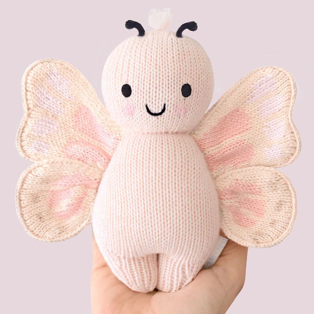 
                  
                    Cuddle + Kind Baby Butterfly (Petal Pink), a hand-knit plush butterfly with soft pink wings and black antennae, displayed in a hand.
                  
                