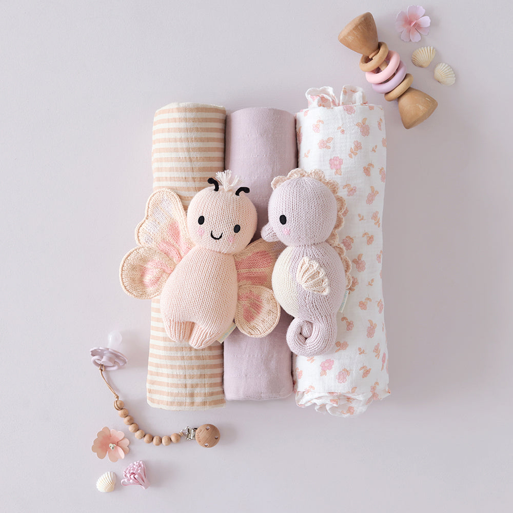 
                  
                    Cuddle + Kind Baby Butterfly (Petal Pink) and Baby Seahorse (Lilac) plush toys placed on rolled muslin swaddles in soft pastel colors.
                  
                