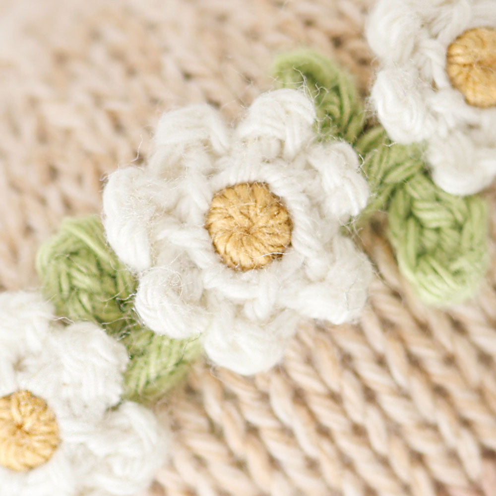 
                  
                    Close-up of Cuddle + Kind Baby Honey Bear (Ivory Floral), showing detailed hand-knit ivory floral crown with green leaves and yellow centers.
                  
                