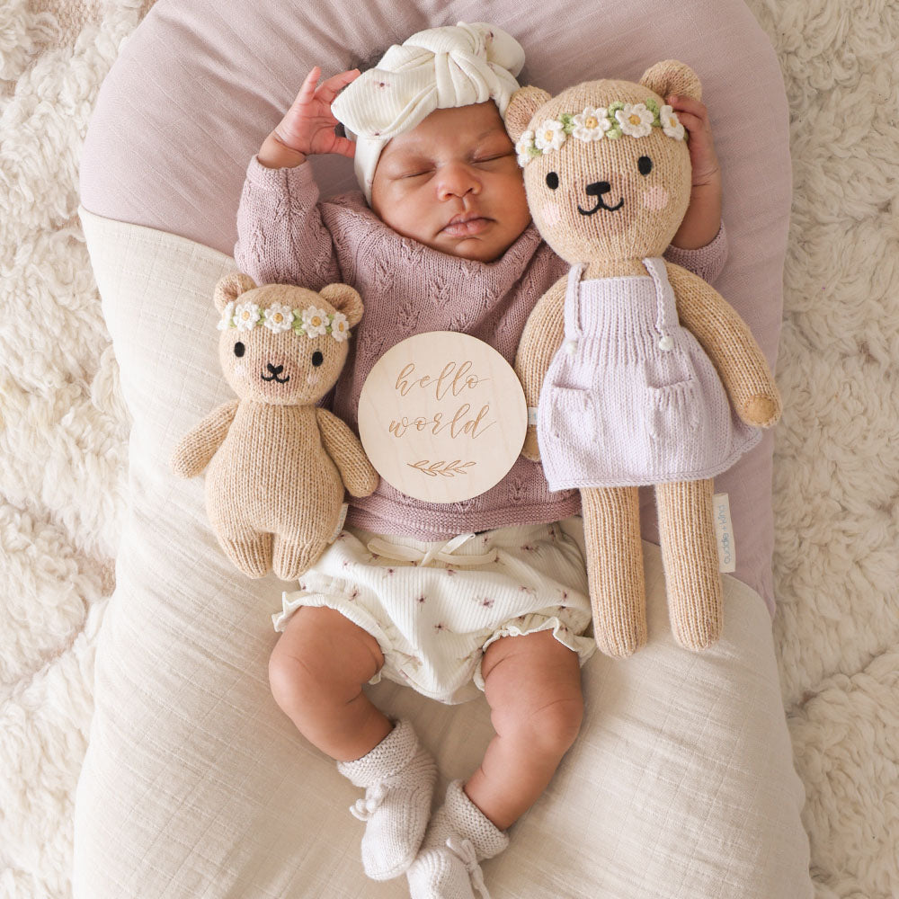 
                  
                    Baby sleeping with Cuddle + Kind Baby Honey Bear (Ivory Floral) and matching larger bear, posed on a cozy blanket with a wooden “Hello World” sign.
                  
                