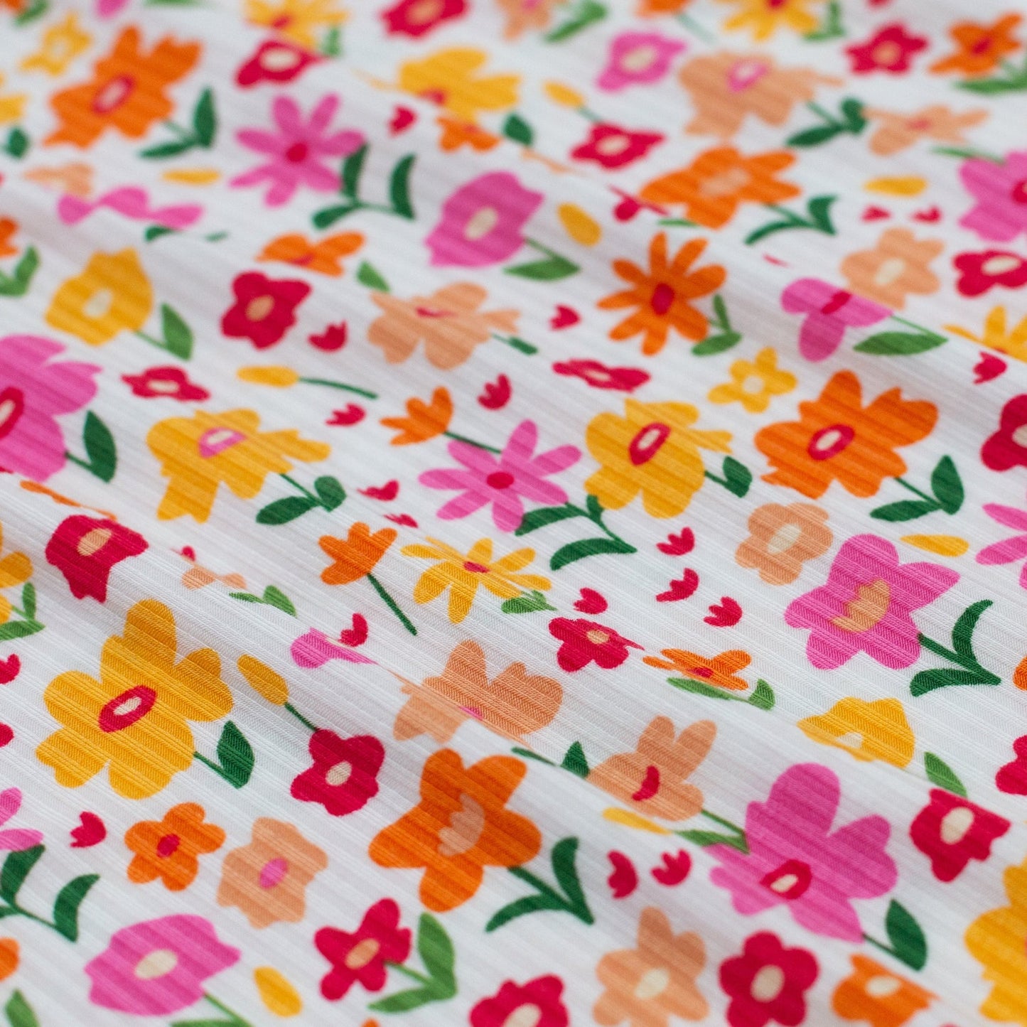 
                  
                    Close-up of ribbed fabric with colorful floral print featuring pink, orange, red, and yellow flowers on a white background.
                  
                