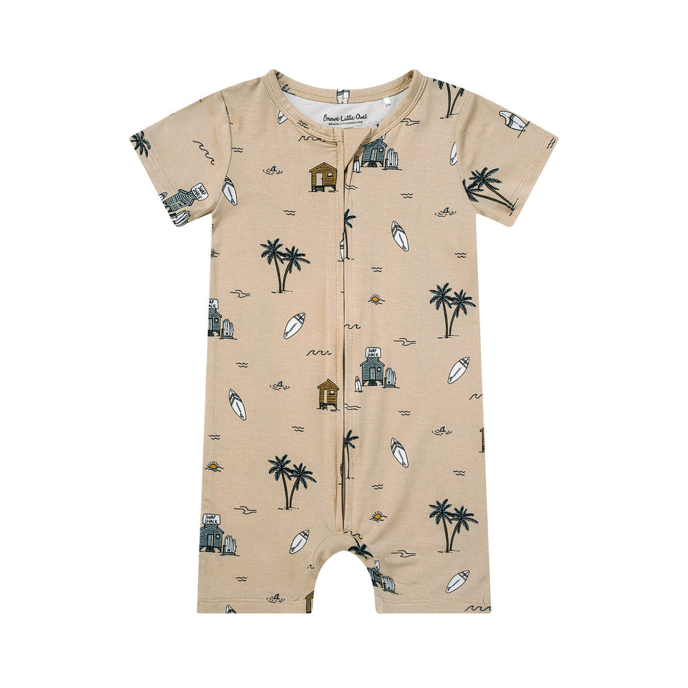 Flat lay of tan Surf Shack zip romper by Brave Little Ones with short sleeves and beach-themed illustrations.