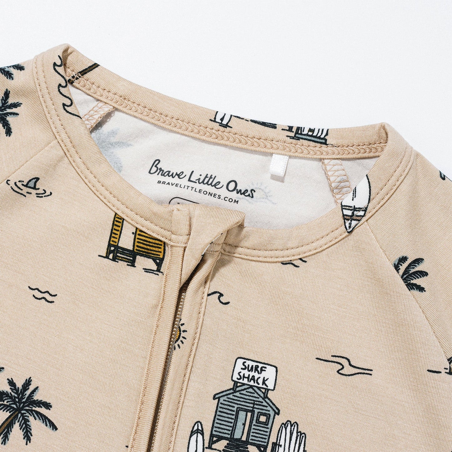 
                  
                    Detailed view of Brave Little Ones Surf Shack summer romper neckline with zipper closure and tan beach print.
                  
                